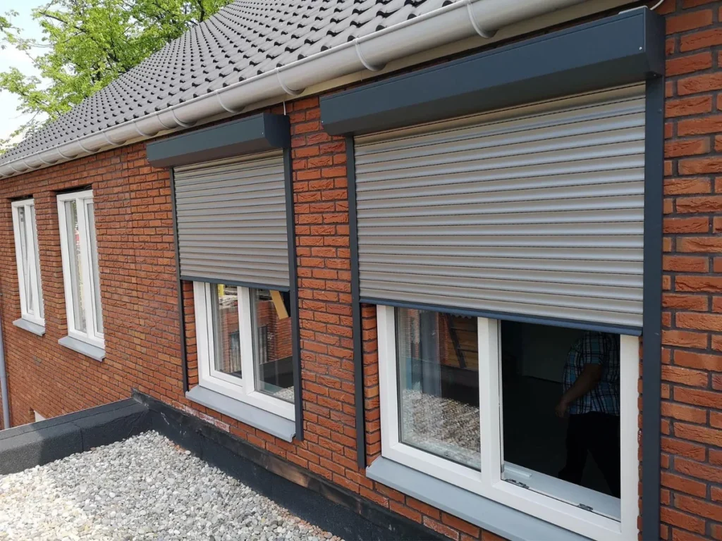 atlasokna-rolluiken-antraciet-halfopen-witte-kozijnen-bakstenen-gevel